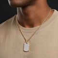 Man wearing a gold chain with a diamond-studded pendant on a plain background